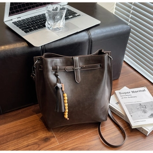 Détail d'un sac seau vintage marron foncé avec pompons et perles sur siège en cuir