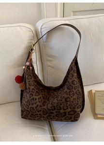 Close-up of leopard print tote bag with fuzzy pom-pom charm on a white fabric surface