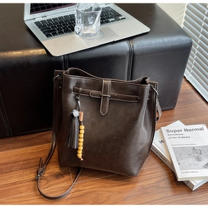 Détail d'un sac seau en cuir marron vintage avec pompon sur un banc texturé
