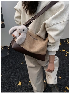 Detail of pleated khaki crossbody bag with smooth brown leather base and plush rabbit charm