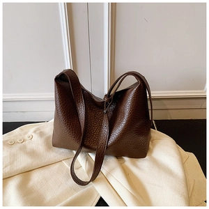 Close-up of deep brown lychee texture on large tote bag placed on a cream blazer