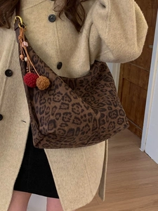 Chic leopard print hobo tote bag with pompom charm shown on shoulder with beige coat