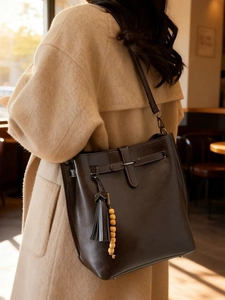 Sac seau rétro en cuir marron foncé avec pompon et perles en bois porté à l'épaule