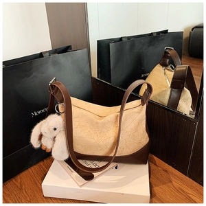 Close-up of beige pleated shoulder bag with brown leather strap and rabbit plush charm
