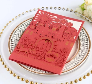 Detail of red laser-cut wedding invitation with gold embossed castle and horse carriage
