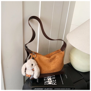 Detail of caramel pleated leather shoulder bag featuring a white plush rabbit pendant