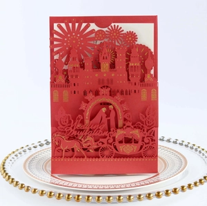 Close-up of red laser-cut wedding invitation featuring a castle and carriage design
