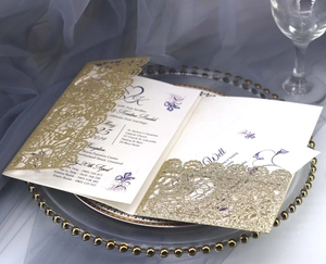 Detail of laser-cut gold glitter wedding invitation with floral lace on elegant dinnerware
