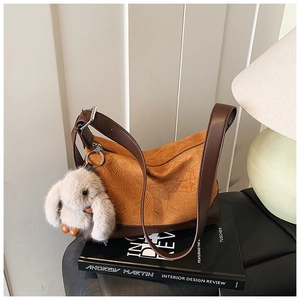 Close-up of caramel pleated dumpling bag with leather strap and plush rabbit charm