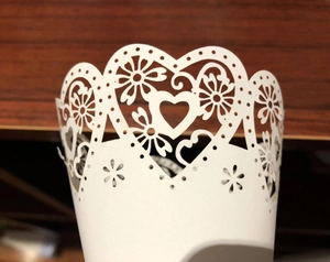 Close-up of white laser-cut paper cone with intricate heart and floral hollow patterns