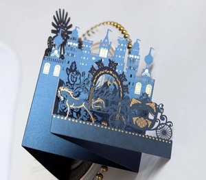 Detail of 3D laser-cut wedding invitation with gold foil castle and carriage on blue paper