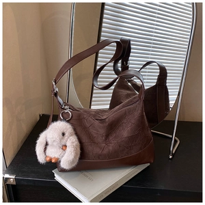 Detail of dark brown pleated hobo bag with a plush bunny charm in a mirror reflection