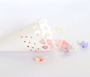 Close-up of laser-cut heart pattern on a white paper wedding petal cone with wavy edges