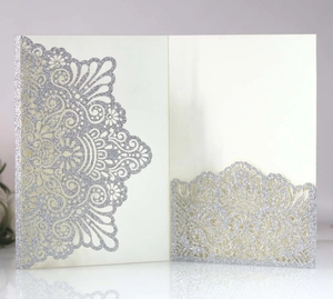 Close-up of laser-cut lace design and silver glitter texture on ivory wedding invitations