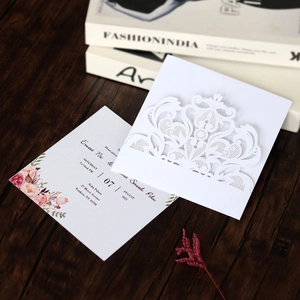 Detailed laser-cut lace wedding invitation with floral inner card on dark wood table