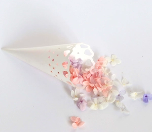 Close-up of laser-cut white heart paper cone filled with romantic dried flower petals