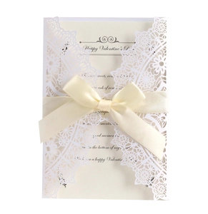 Detail of laser-cut floral invitation with creamy white paper and beige silk ribbon bow