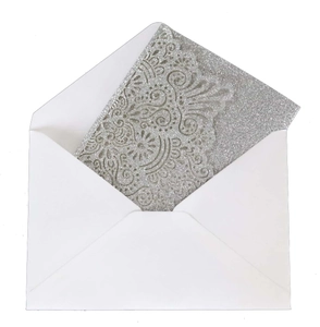 Detail of silver glitter laser cut wedding invitation with intricate floral patterns and envelope