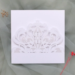 Close-up of white laser-cut wedding invitation card with intricate damask lace patterns