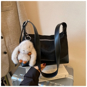 Detail of black canvas tote bag featuring leather base, silver zipper, and plush bunny charm