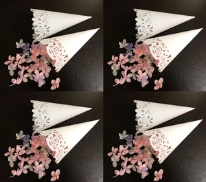Detailed laser-cut white rose confetti cones with pink flower petals on wood surface