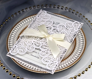Laser-cut white wedding invitation with silk bow and silver glitter border on decorative plate