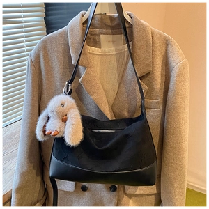 Detail of pleated black handbag featuring a plush rabbit charm on beige blazer setup