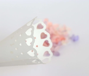 Close-up of white laser-cut heart pattern wedding confetti cone with hollow details