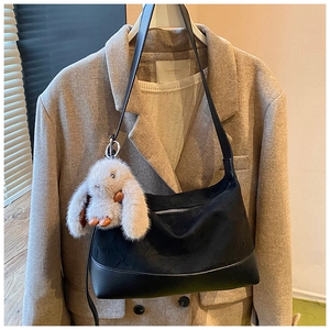 Detail of black pleated crescent bag with a cute fluffy bunny charm on a wool coat