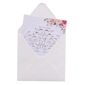 Close-up of laser-cut white lace wedding invitation with floral insert and envelope