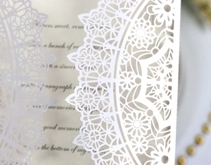 Macro shot of intricate laser-cut floral lace patterns on elegant white wedding invitation