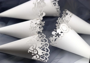 Detail of white laser-cut paper cones with floral and heart patterns for wedding petals