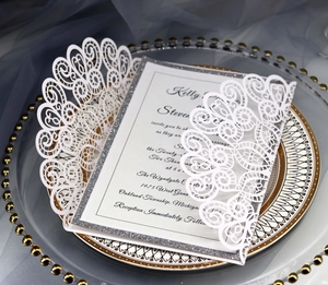 Detail of laser-cut invitation featuring white floral patterns and silver glitter border