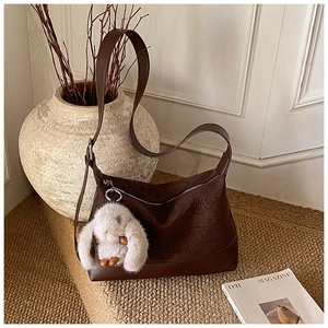 Detail of dark brown pleated hobo bag with contrast stitching and plush rabbit charm