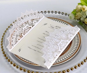 Detail of laser-cut cream wedding invitation with intricate lace hollow-out design