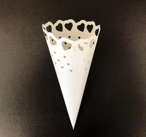 Detail of white laser-cut paper cone with hollow heart patterns for wedding flower petals
