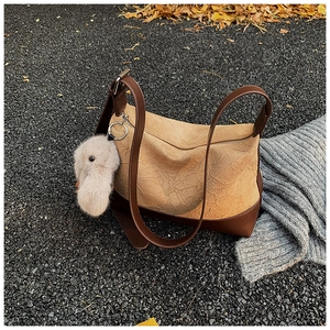 Close-up of two-tone pleated shoulder bag with a plush rabbit charm on outdoor asphalt