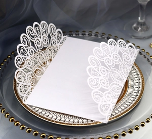 Detailed laser-cut white lace invitation card elegantly placed on luxury dinner plates