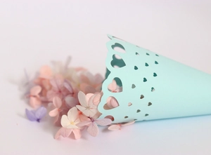 Detail of laser-cut heart pattern on a mint green paper cone filled with dried flower petals