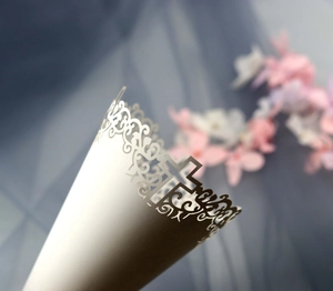 Close-up of laser-cut white wedding paper cone with intricate cross lace design