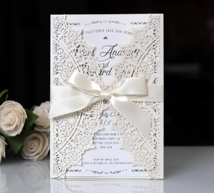 Detailed macro view of laser-cut ivory wedding invitation with elegant satin ribbon bow