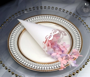Detail of white laser-cut lace wedding paper cone with dried petals on an elegant plate