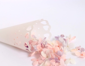 Close-up of white heart-shaped hollow paper cone filled with colorful wedding confetti petals