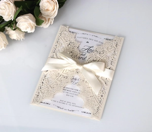 Detail of laser-cut cream wedding invitation with ivory ribbon bow and elegant lace patterns