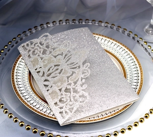 Close-up of silver glitter laser-cut lace wedding invitation on a decorative plate