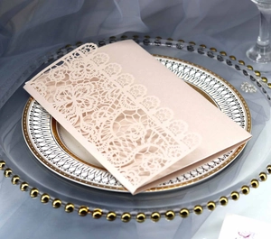 Close-up of laser-cut lace wedding invitation in champagne pink with pearl paper texture