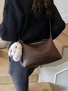 Brown pleated dumpling shoulder bag with plush rabbit charm shown on a model's back