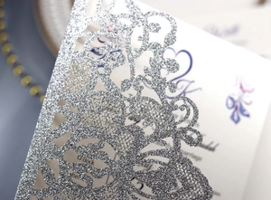 Macro shot of silver glitter laser-cut vine patterns on a wedding invitation cover