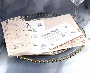 Macro view of laser-cut lace wedding invitation with floral insert and pink envelope