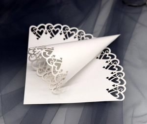 Detailed macro view of laser-cut white paper confetti cone with elegant heart lace patterns